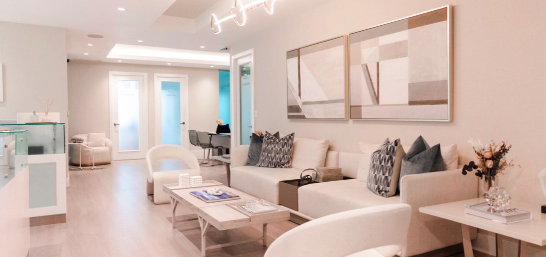 Image of a clean and modern clinic waiting room with table and chairs and a reception desk on the left.